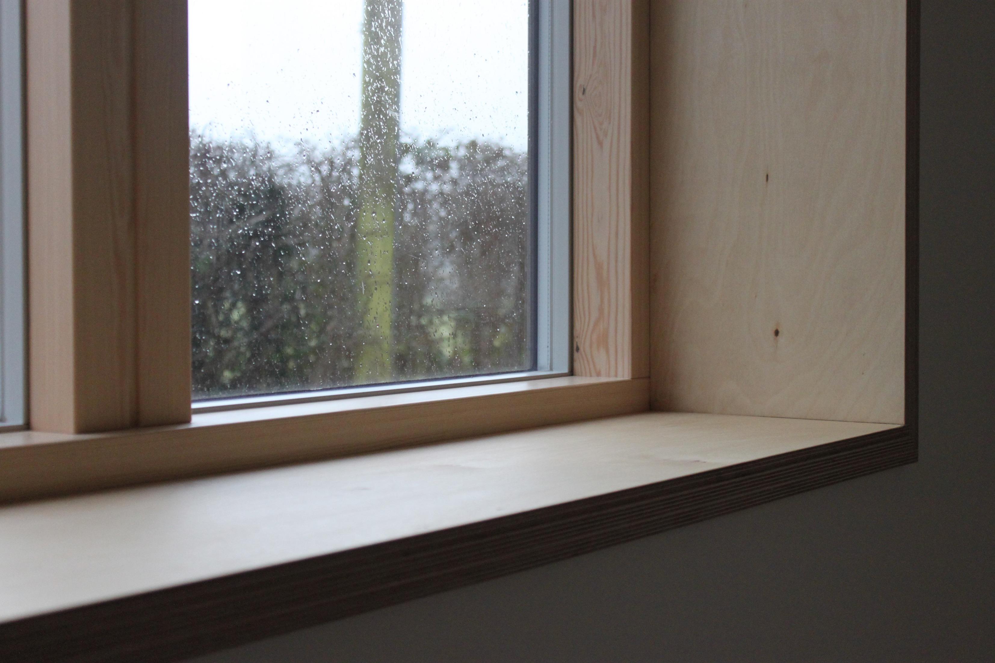 A removable plywood insert panel with a simple 1x2 wood frame on a workbench, cut to fit a window opening